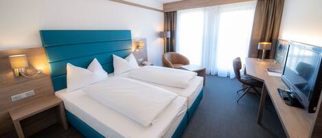 A hotel room with a large bed, a desk with a TV, and a chair.