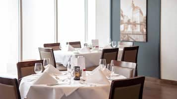 A dining area with tables set for four, each with white tablecloths, chairs, and glassware.
