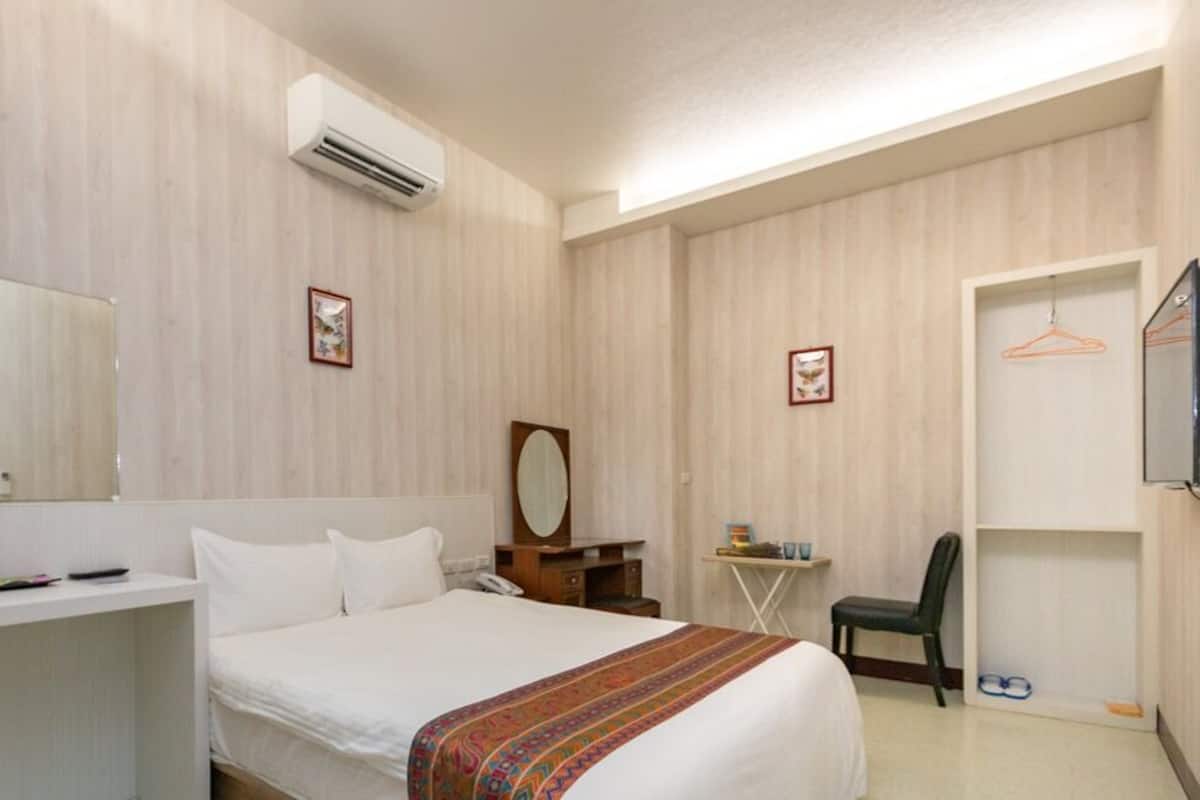 A hotel room with a bed, bedside table, mirror, and a small desk with a chair.