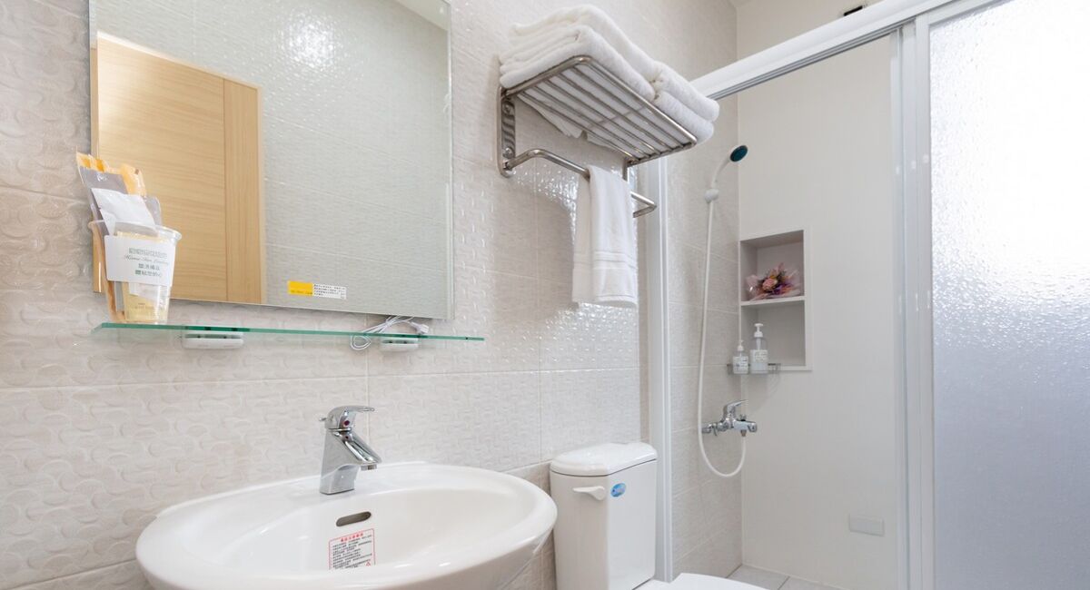Ein Badezimmer mit Waschbecken, Spiegel, Handtuchhalter, Dusche und Toilette.