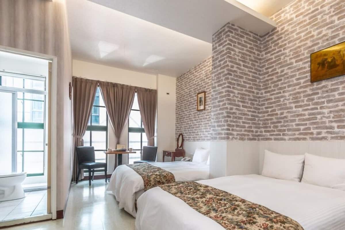 A hotel room with two beds, a desk, and a chair.