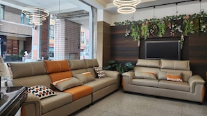 Ein moderner Wohnbereich mit einem Ecksofa und einem kleinen Sofa, beide mit dekorativen Kissen. Hängende Pflanzen und ein flachbildfernseher an der Wand.