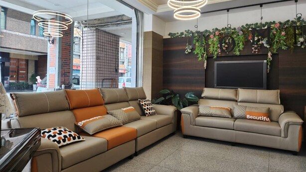 A modern living area with a sectional sofa and a smaller sofa, both with decorative pillows. There are hanging plants and a flat-screen TV mounted on the wall. - Jia-Jia Business Hotel (Luodong)