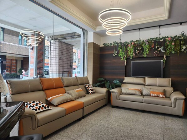 A modern living area with a sectional sofa and a smaller sofa, both with decorative pillows. There are hanging plants and a flat-screen TV mounted on the wall. - Jia-Jia Business Hotel (Luodong)