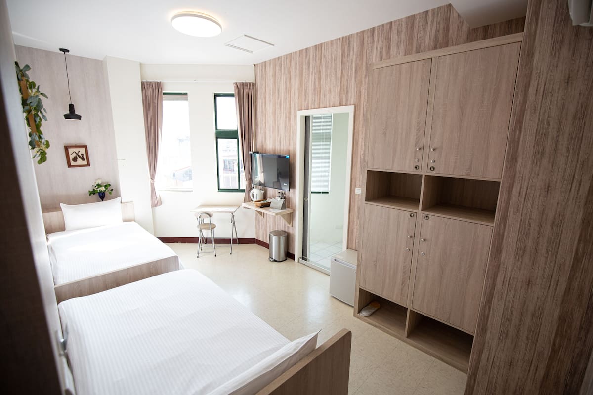 A hotel room with two beds, a desk, a chair, a TV, and a wardrobe.
