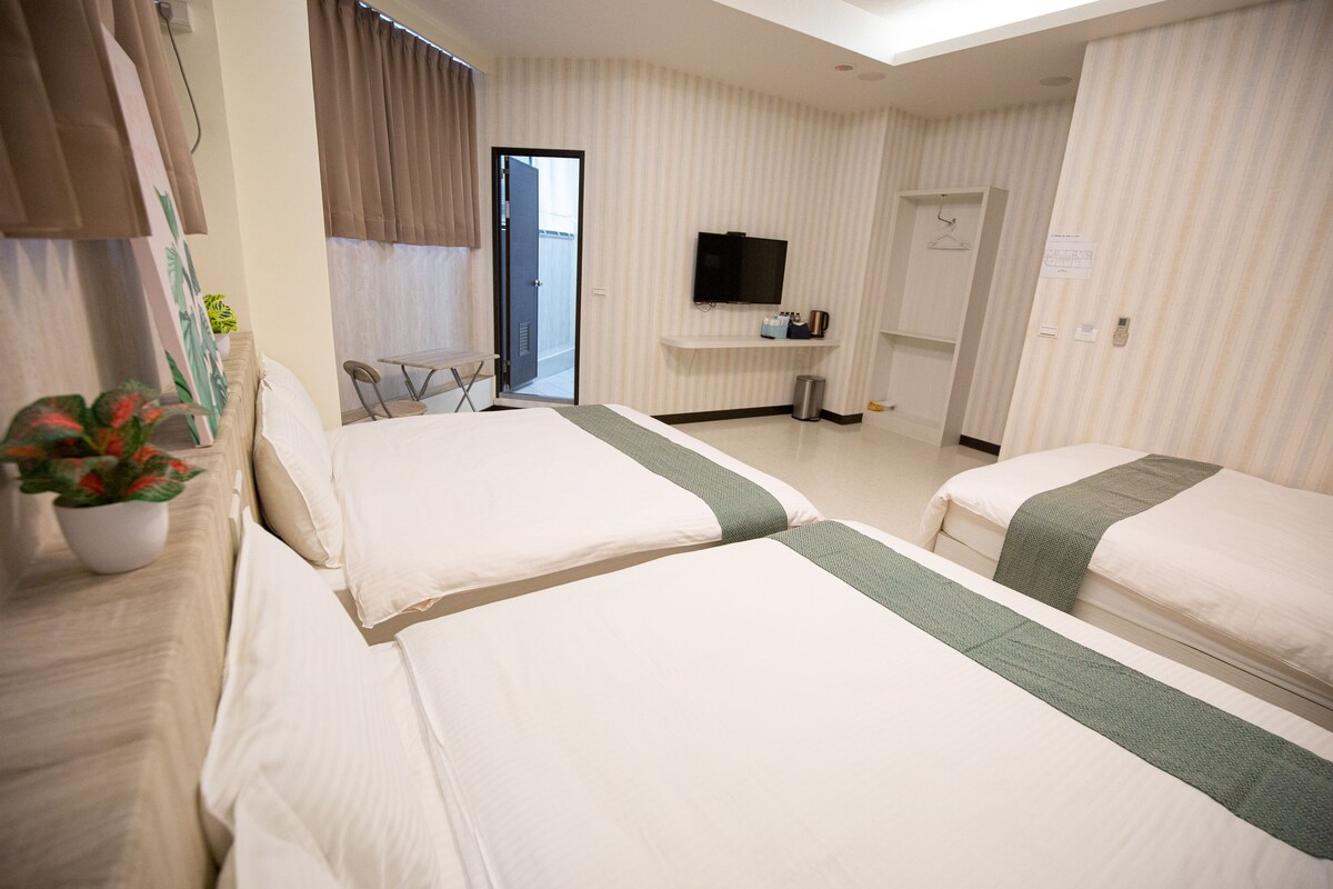 A hotel room with two beds, a TV, a small table, and a potted plant.