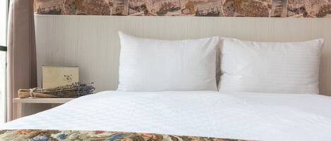 Habitación de hotel con una cama, dos almohadas, una mesita de noche con lámpara y una colcha de estampado floral.