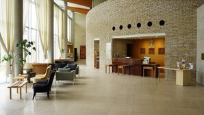 Eine geräumige Lobby mit Backsteinwand, einer Rezeption, einer Sitzecke und großen Fenstern.