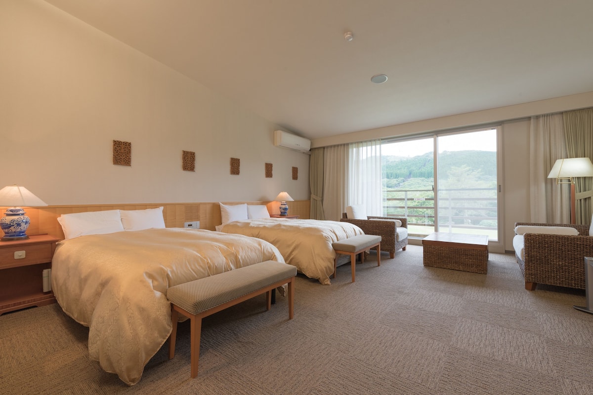 Een hotelkamer met twee bedden, een zithoek en een groot raam met uitzicht op het omliggende landschap.