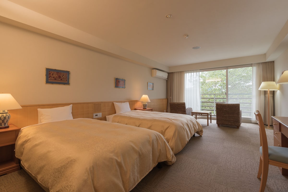 Een hotelkamer met twee bedden, een bureau, een stoel en een raam met gordijnen.