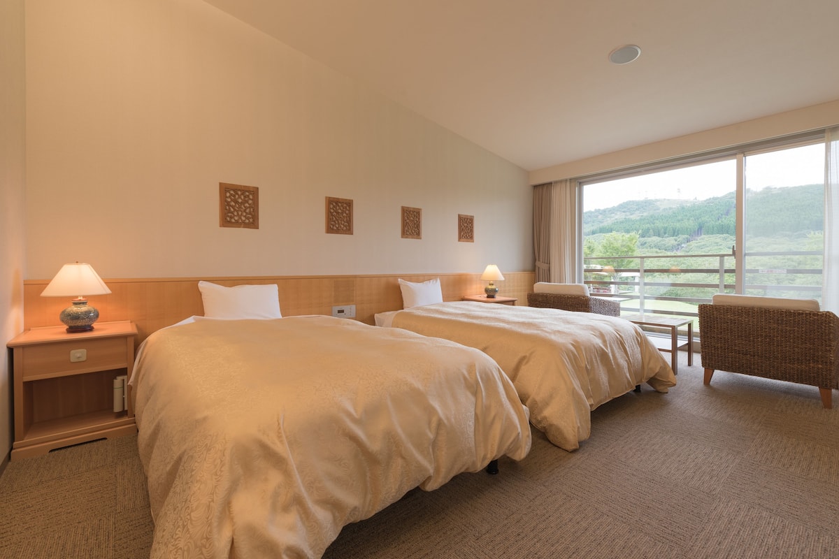 Een hotelkamer met twee bedden, een stoel, een klein tafeltje en uitzicht op de omgeving.