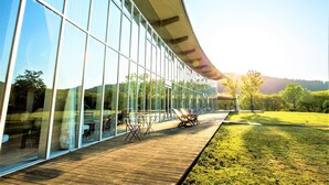Ein modernes Gebäude mit großen Glasfenstern und einer Holzterrasse mit Außenmöbeln.