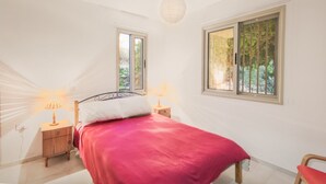 Un dormitorio con una cama, dos mesitas de noche, una lámpara, una ventana y una silla.