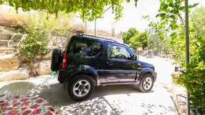 Un SUV negro estacionado en una zona sombreada con un muro de piedra y follaje de fondo.