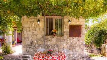 Un edificio de piedra con una ventana y una mesa para dos bajo un árbol.
