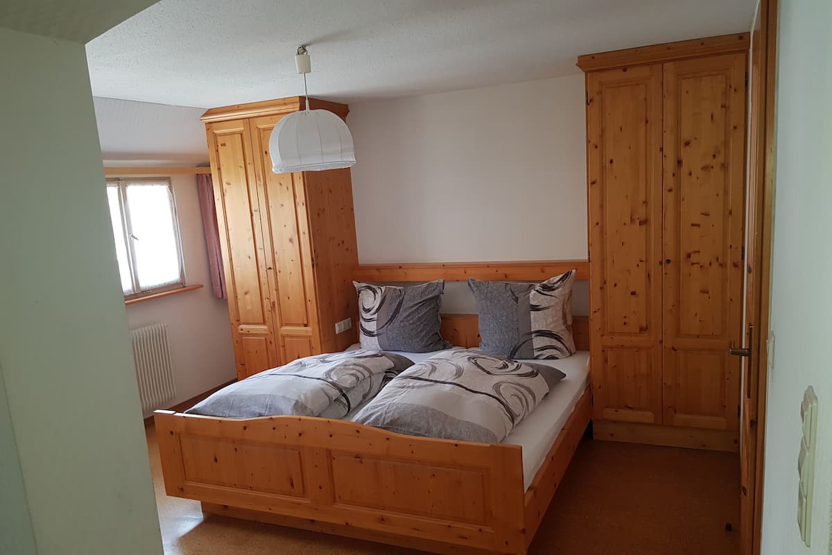 A wooden bed with a headboard, a hanging light fixture, and a window with curtains.