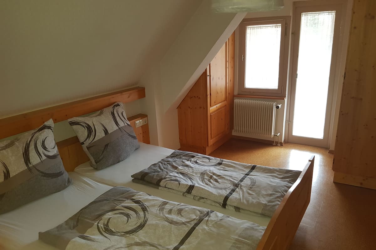 A bedroom with two beds, wooden headboards, and a window with a view.