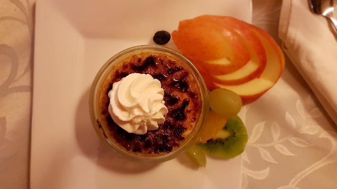 Un postre con crema batida, una rodaja de manzana y kiwi en un plato.