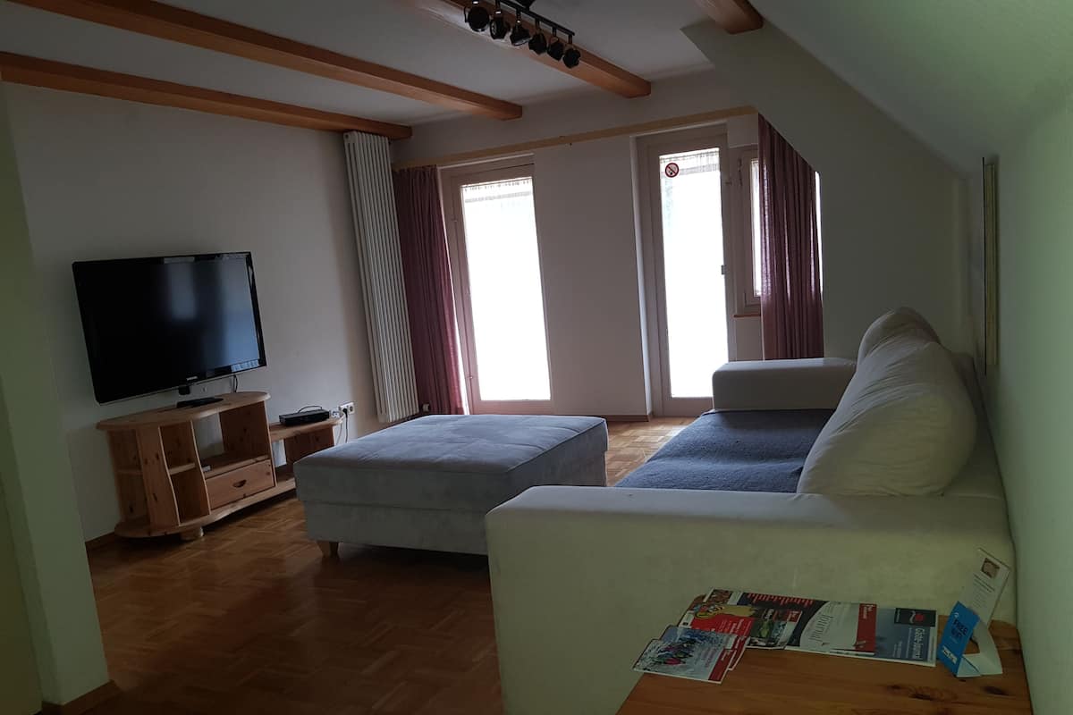 A living room with a flat-screen TV, a wooden entertainment unit, a sofa, and a table with magazines.