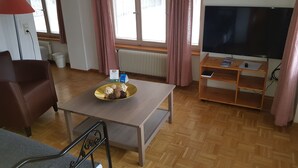 A living room with a sofa, a table with a bowl of snacks, a TV on a stand, and a radiator. - Antico mulino (Todtmoos)