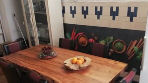 A wooden dining table with chairs, a bowl of fruit, and a cabinet in a room with tiled walls. - Privatzimmer Hagen (Hagen)