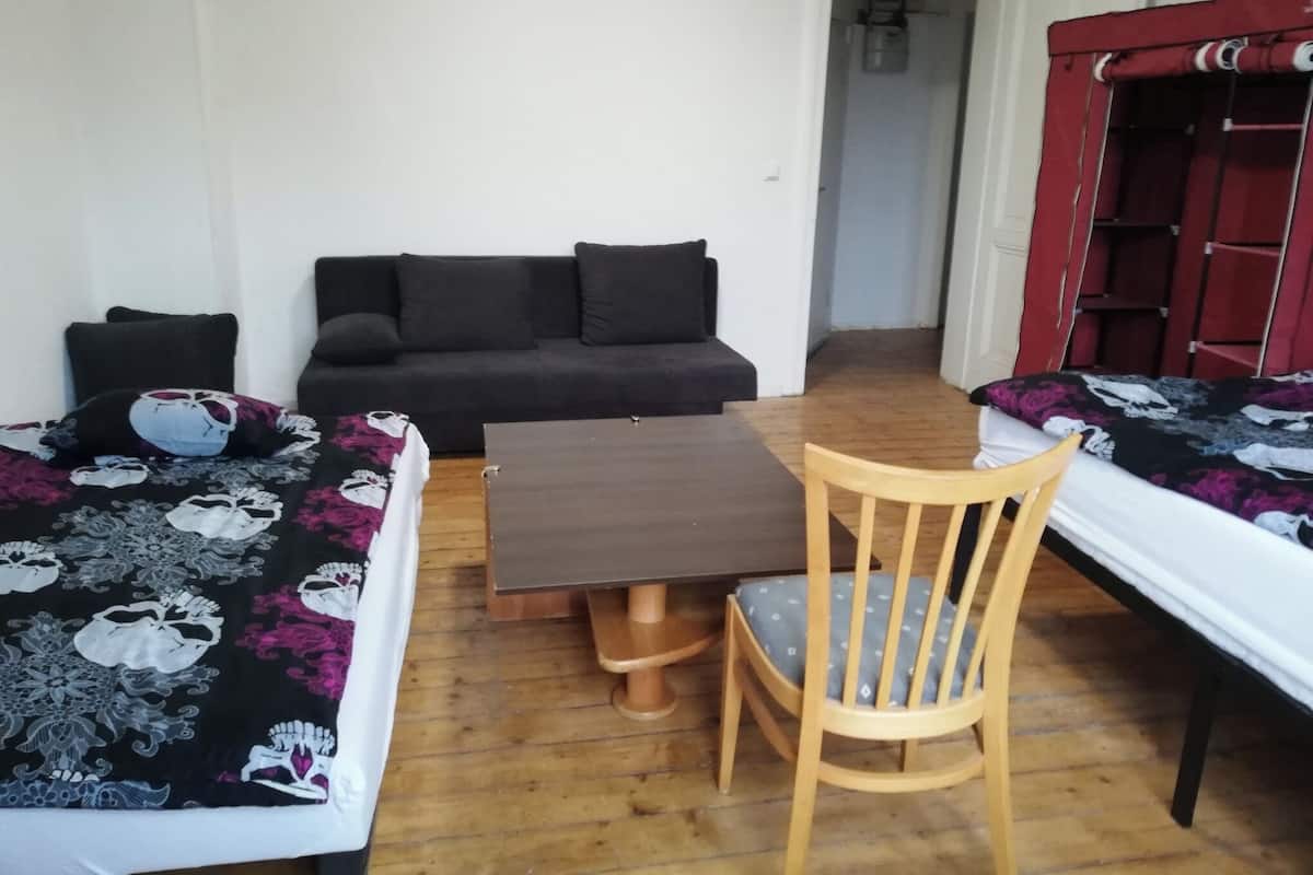 Quarto com duas camas, uma mesa de madeira, uma cadeira, um sofá e um guarda-roupa.