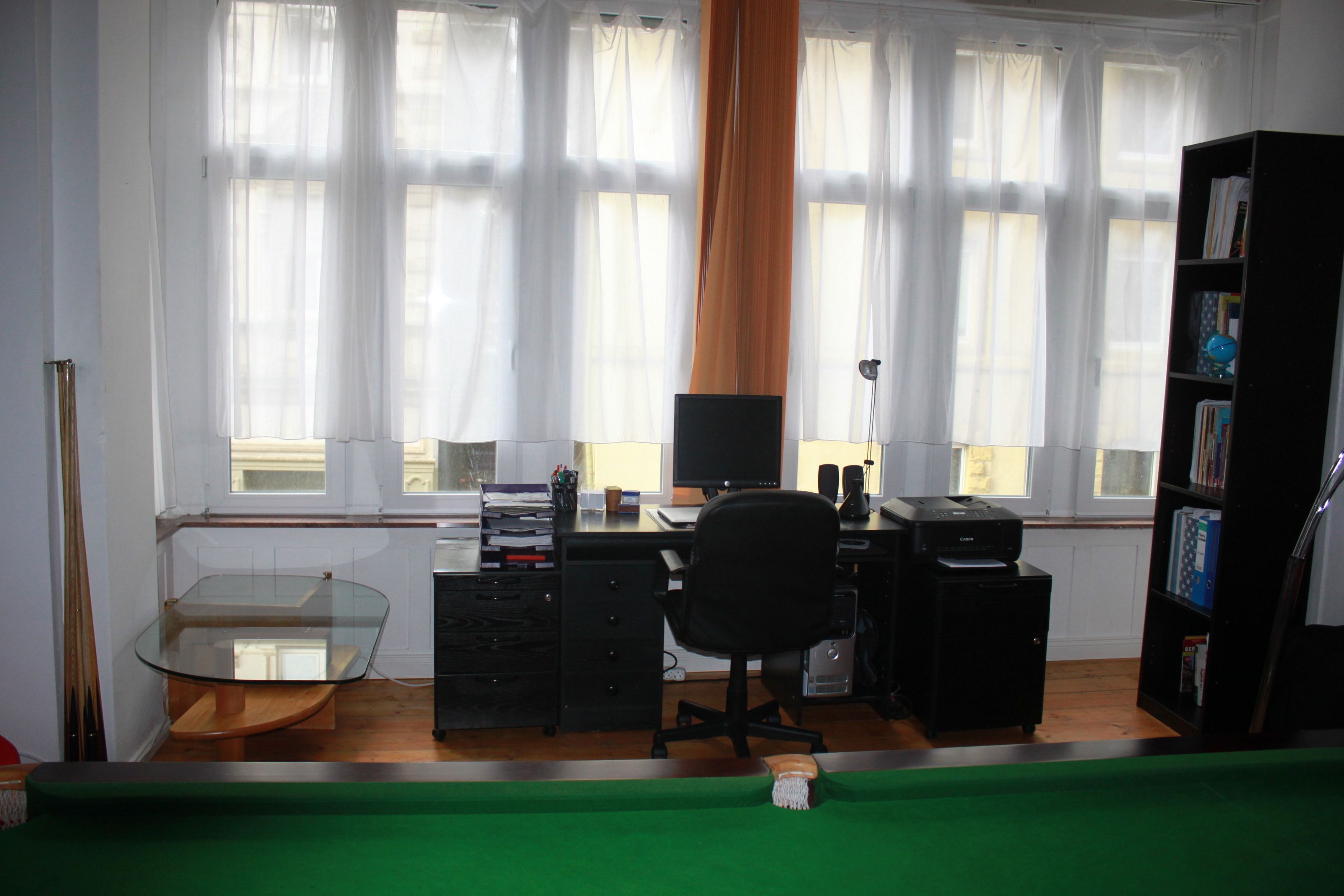 A room with a glass-top table, a black office chair, a bookshelf, and a desk with a computer and printer.