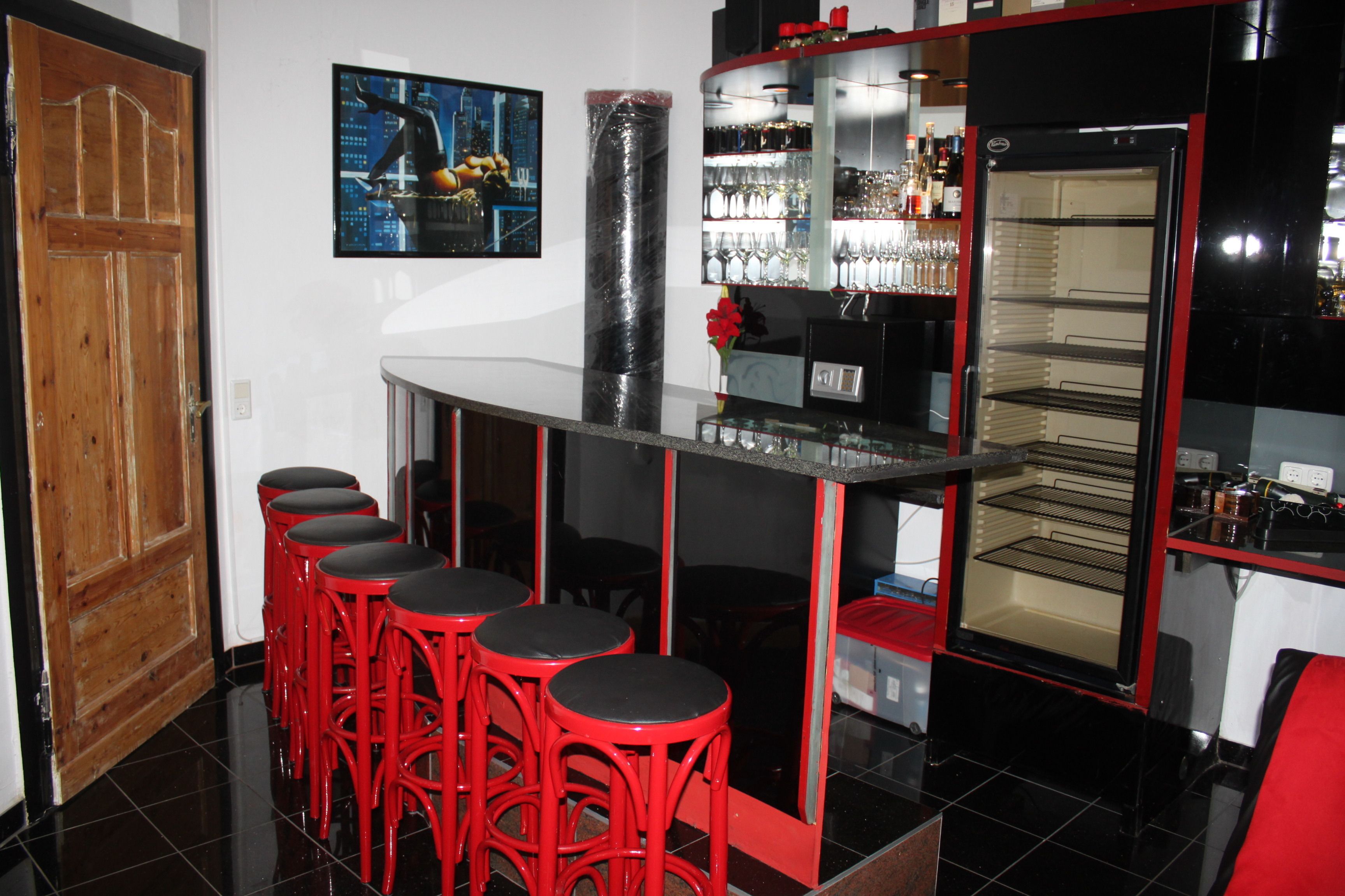A bar area with red stools, a refrigerator, and a wine rack.