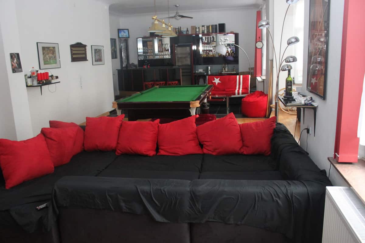 Uma sala de estar com mesa de bilhar, almofadas vermelhas e uma bandeira vermelha na parede.