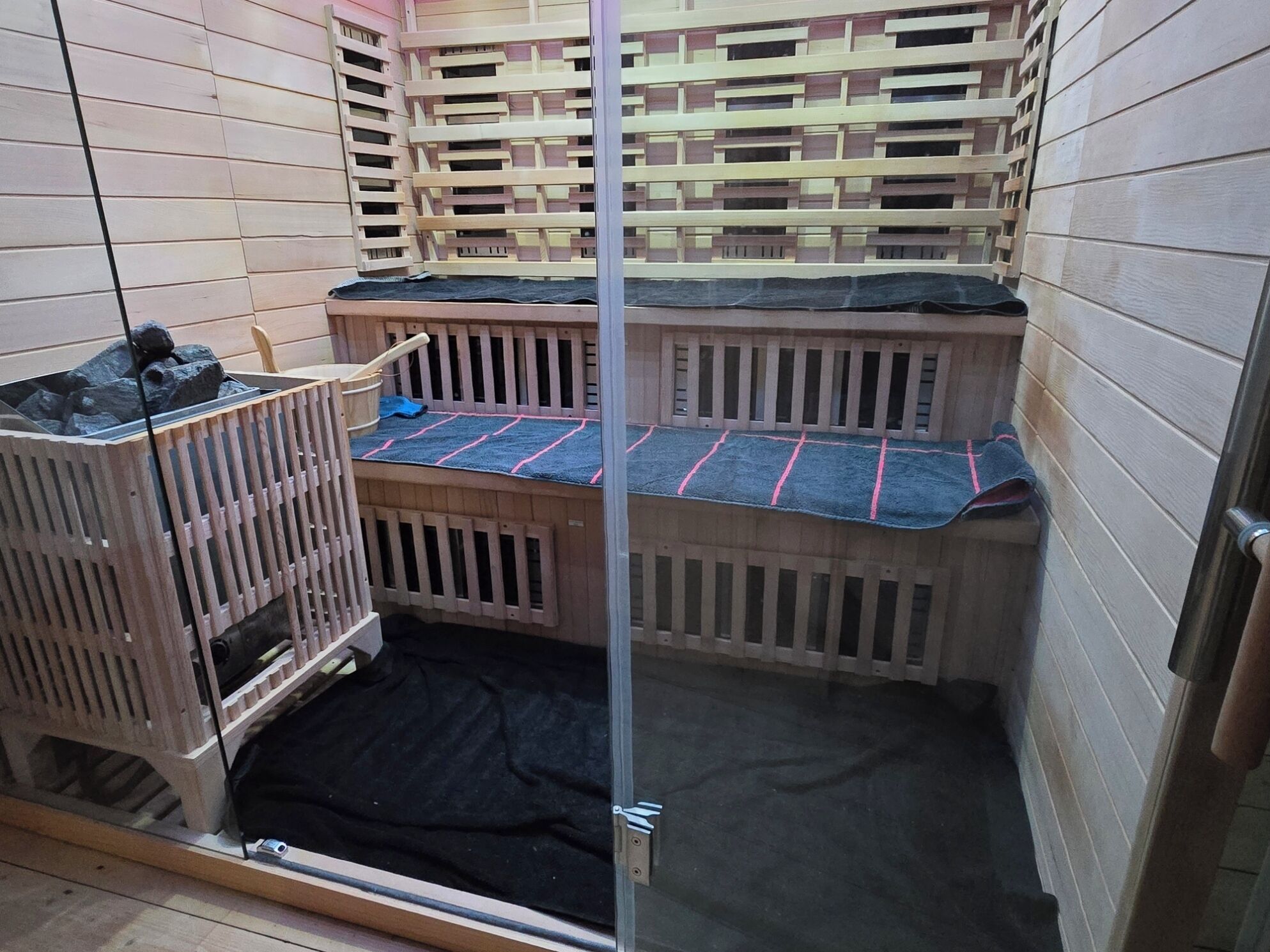 A small, enclosed room with two wooden bunk beds, a black mat on the floor, and a wooden crib.