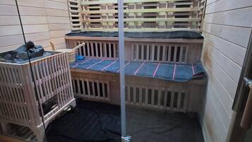 A small, enclosed room with two wooden bunk beds, a black mat on the floor, and a wooden crib.