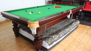 A pool table with balls, a sofa, and a fur-covered ottoman in a room with wooden flooring. - Privatzimmer Hagen (Hagen)