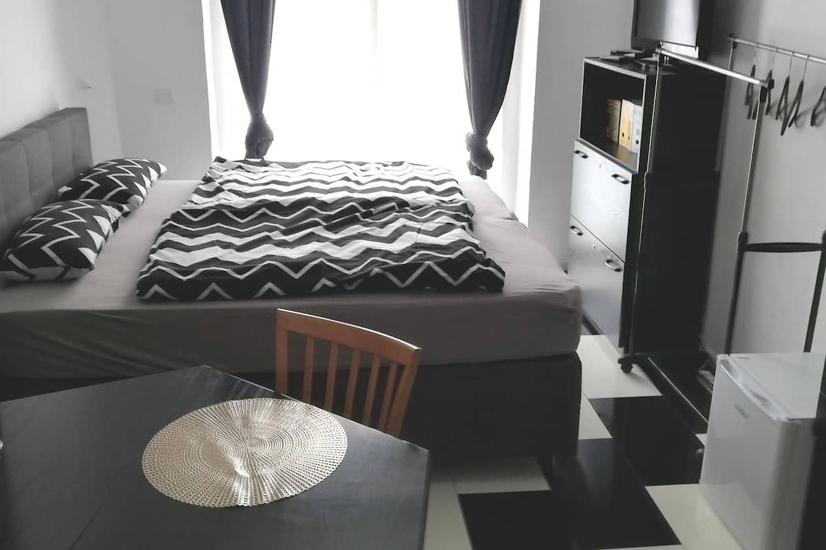 Quarto pequeno e moderno com uma cama, uma mesa e uma televisão.