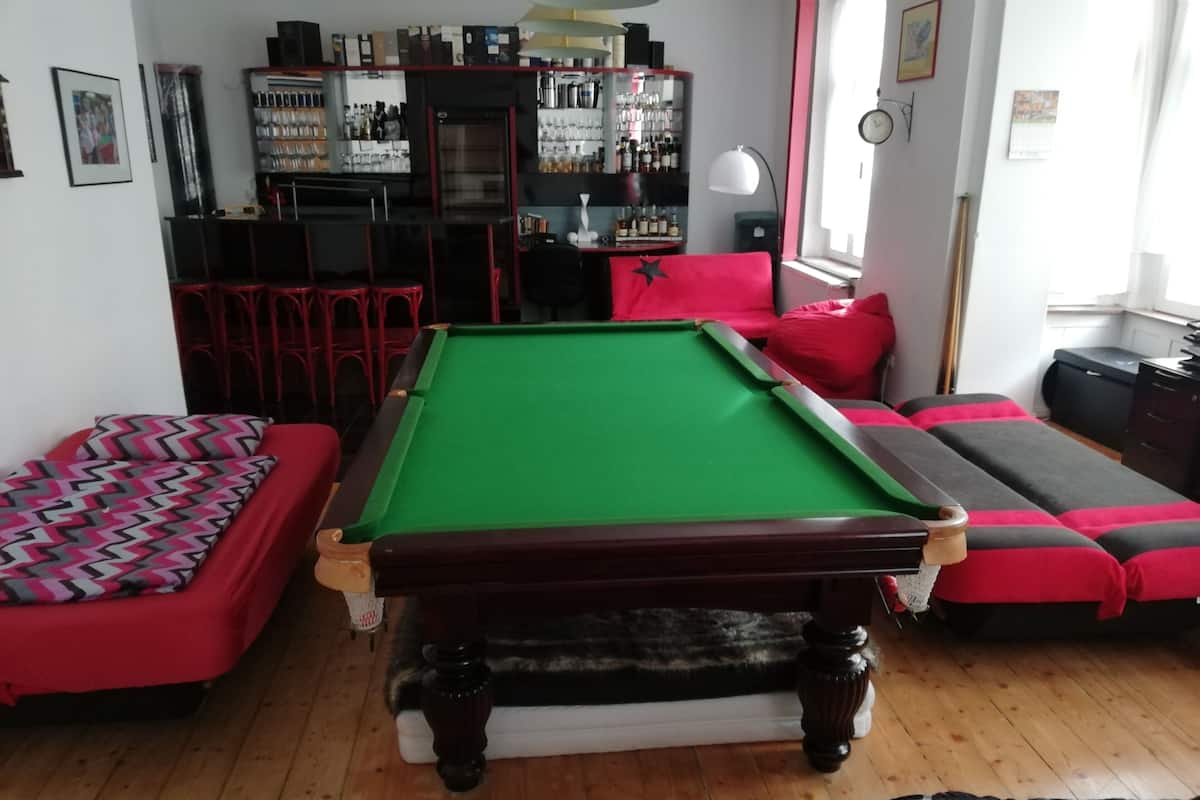 Uma mesa de bilhar em um espaço com área de bar, mobiliário vermelho e preto, e piso de madeira.