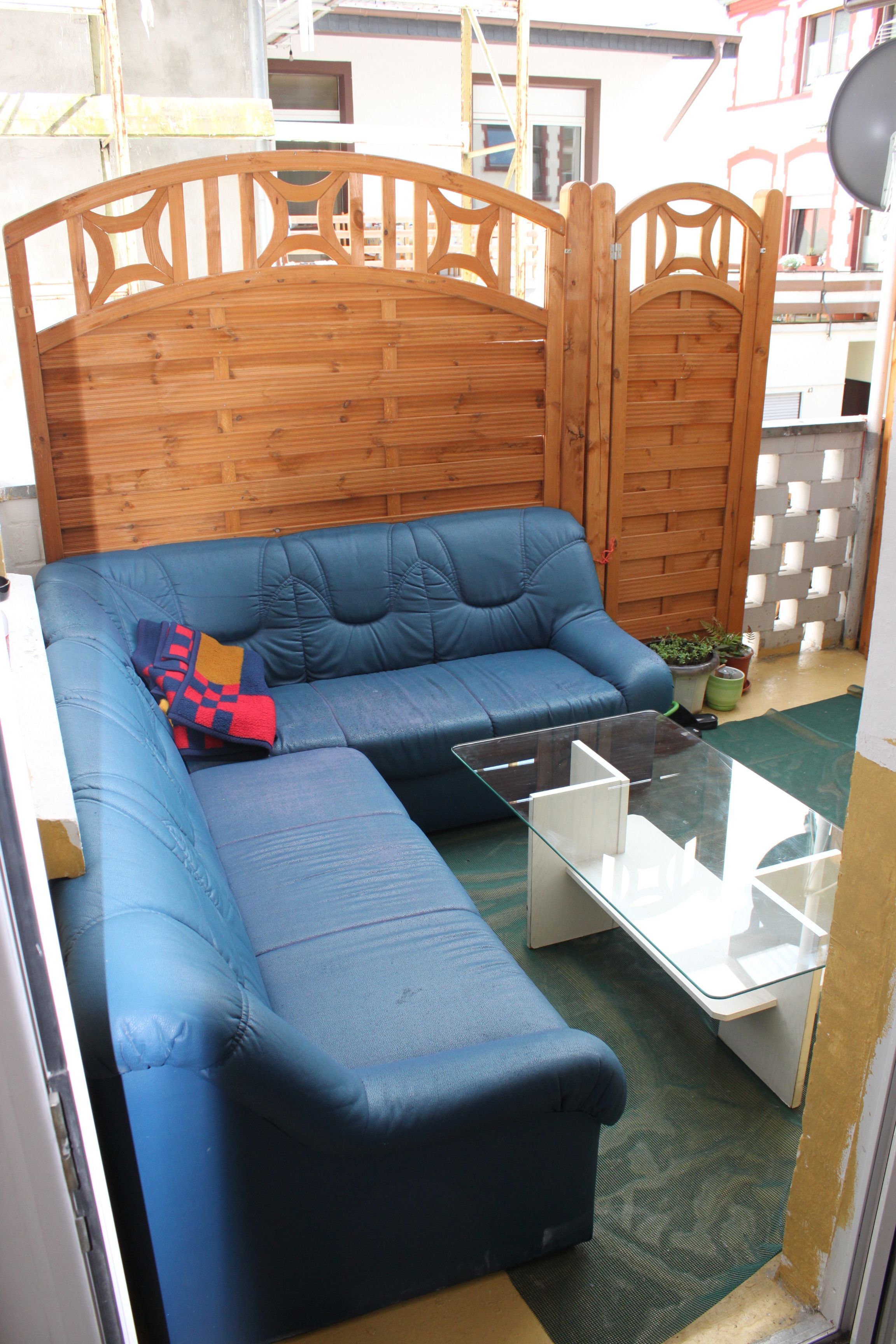Un canapé bleu avec une tête de lit en bois, une table basse en verre et une petite plante en pot.