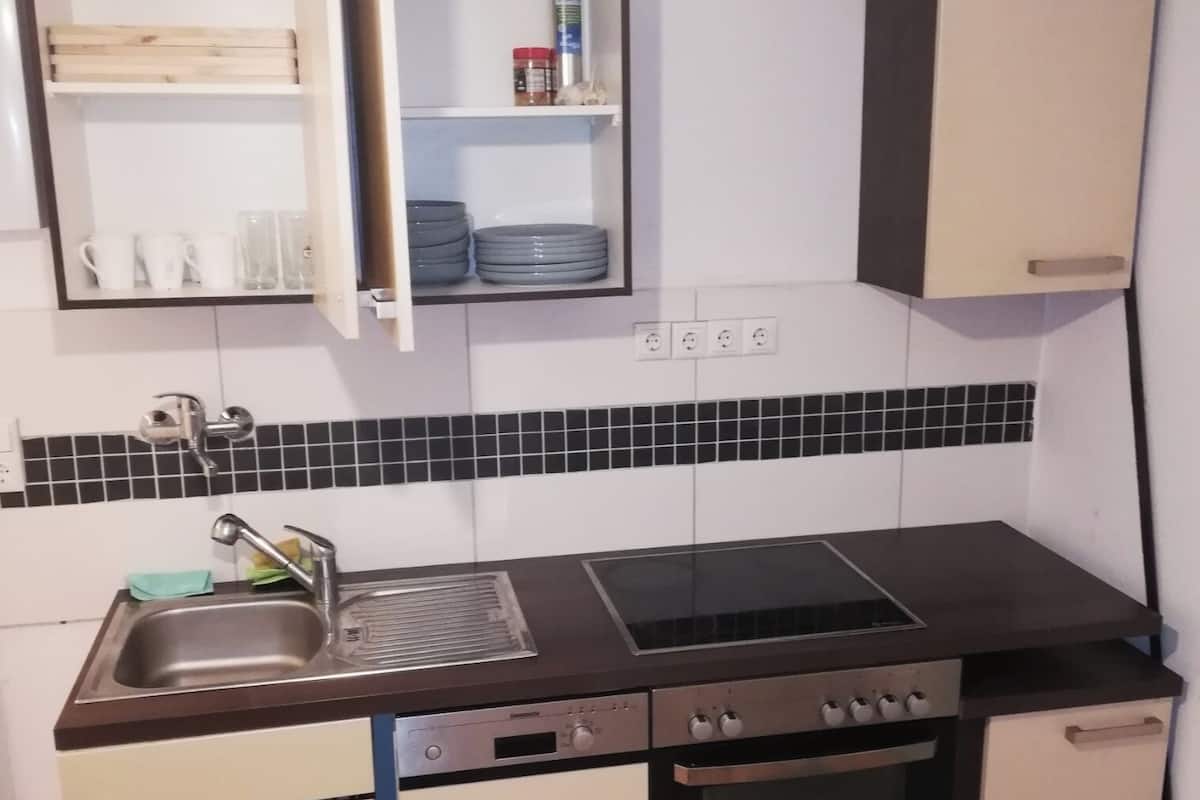 Uma cozinha compacta com pia, fogão, forno e um pequeno armário com louças.