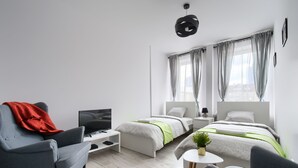 A modern hotel room with a grey sofa, a TV, a bed with green bedding, and a small table with a plant. - Chmielna Premium z dwoma sypialniami (Warsaw)