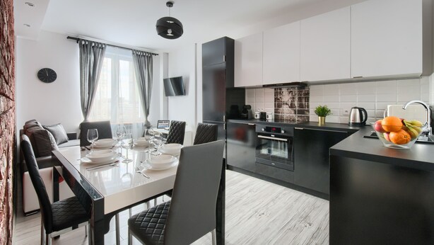 A modern kitchen with black cabinets, a built-in oven, and a coffee maker. - Chmielna Premium z dwoma sypialniami (Warsaw)