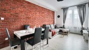 A modern living space with a brick wall, a dining area with a table set for two, a sofa, and a small side table. - Chmielna Premium z dwoma sypialniami (Warsaw)