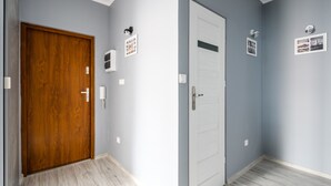 A hallway with a wooden door and a white door, both with light switch and intercom panels. - Chmielna Premium z dwoma sypialniami (Warsaw)