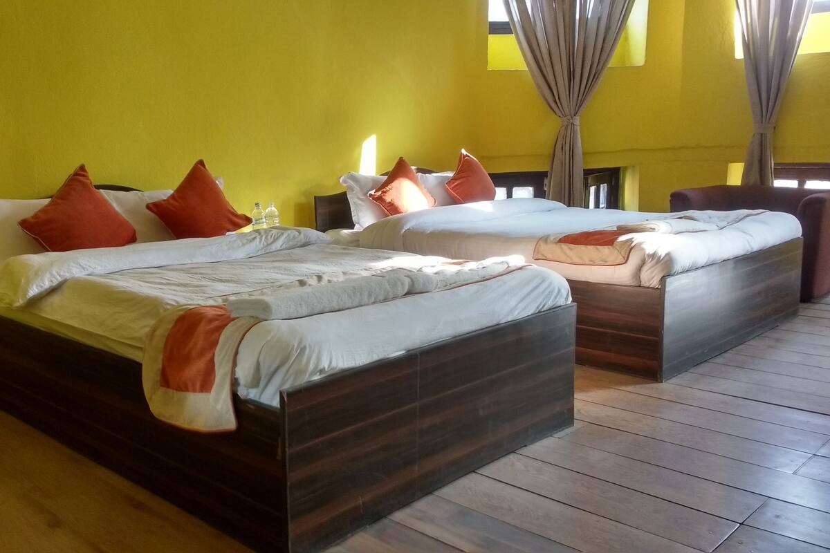 Camera d'albergo con due letti, pavimento in legno e pareti gialle.