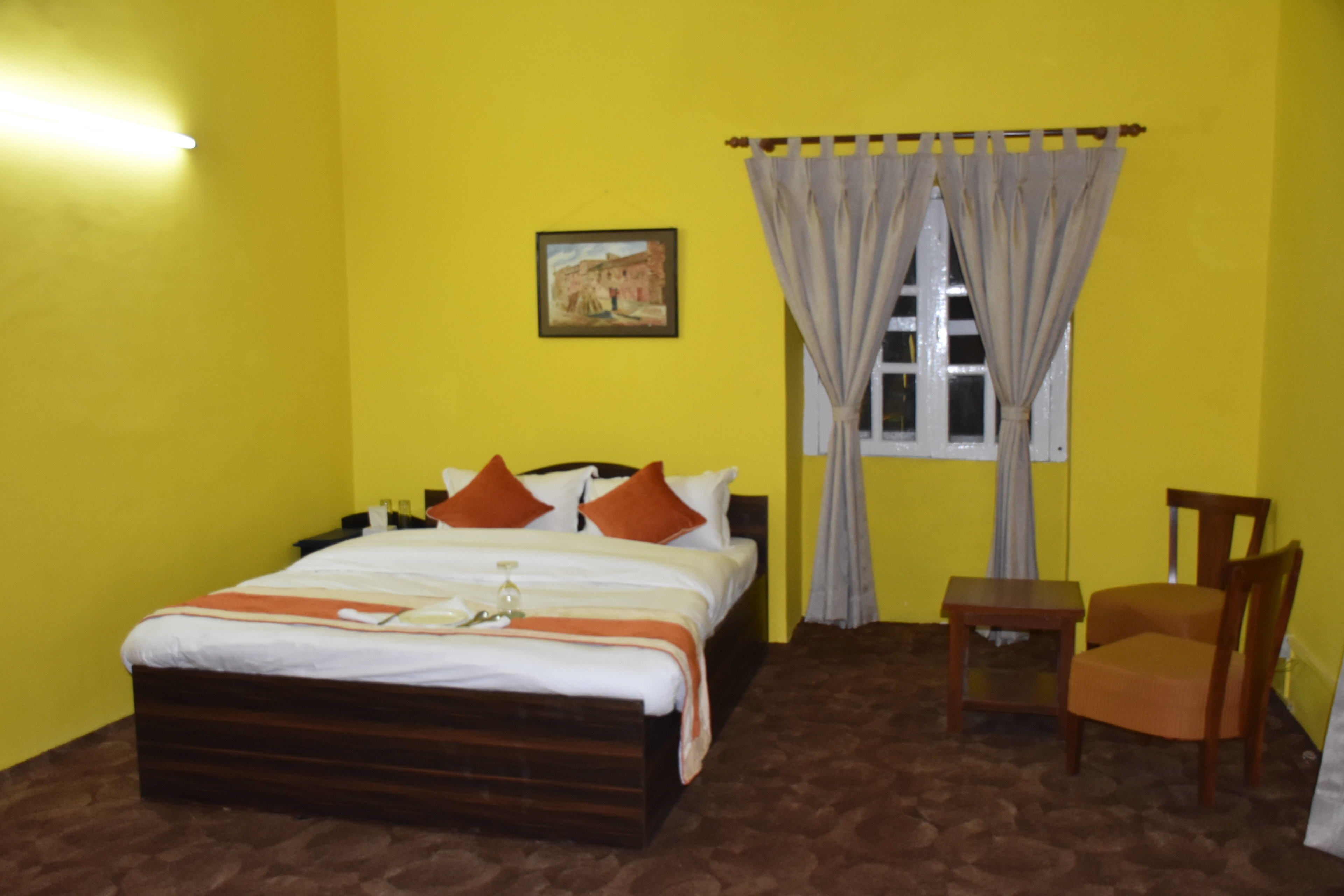 A room with a bed, a chair, a small table, a window with curtains, and a painting on the wall.