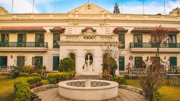 A building with a central fountain, multiple balconies, and a garden with potted plants. - Yellow Durbar Apartment and Lounge (Lalitpur)