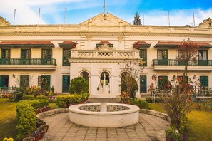 A building with a central fountain, multiple balconies, and a garden with potted plants. - Yellow Durbar Apartment and Lounge (Lalitpur)