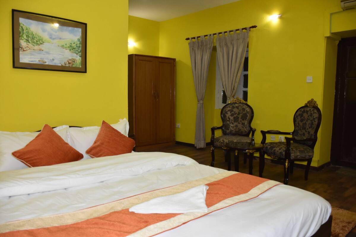 Una camera d'albergo con un letto, due poltrone, un armadio in legno e un quadro appeso al muro.