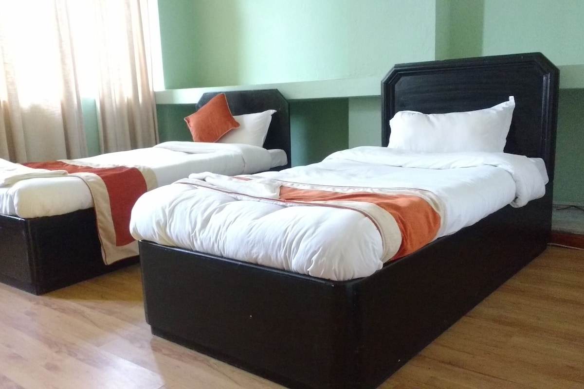 Two single beds with black frames and white bedding, a wooden floor, and a window with curtains.