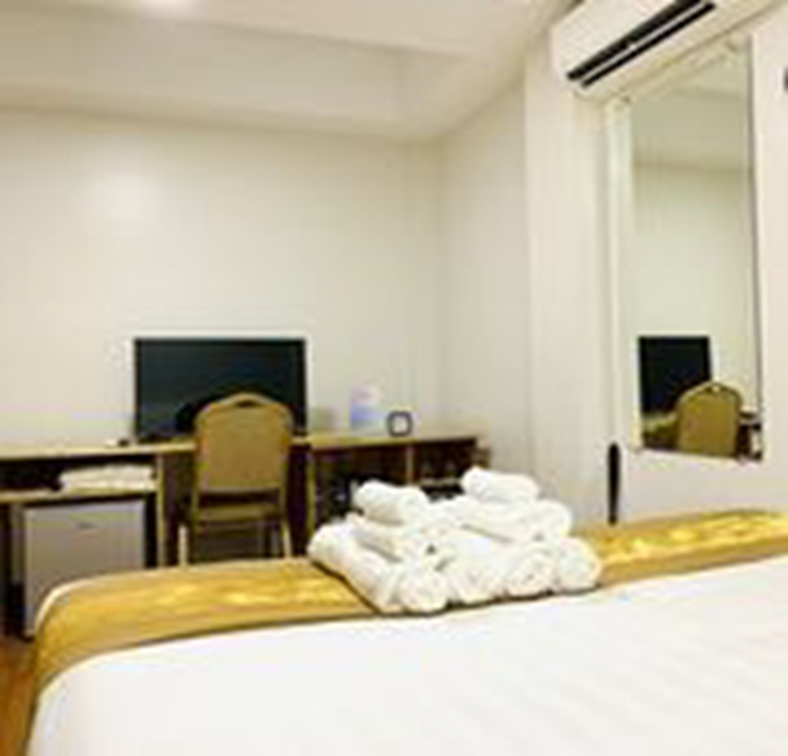 Una habitación de hotel con cama, escritorio, silla, televisor y espejo.