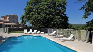 Una piscina con sillones de descanso y un edificio de piedra al fondo.