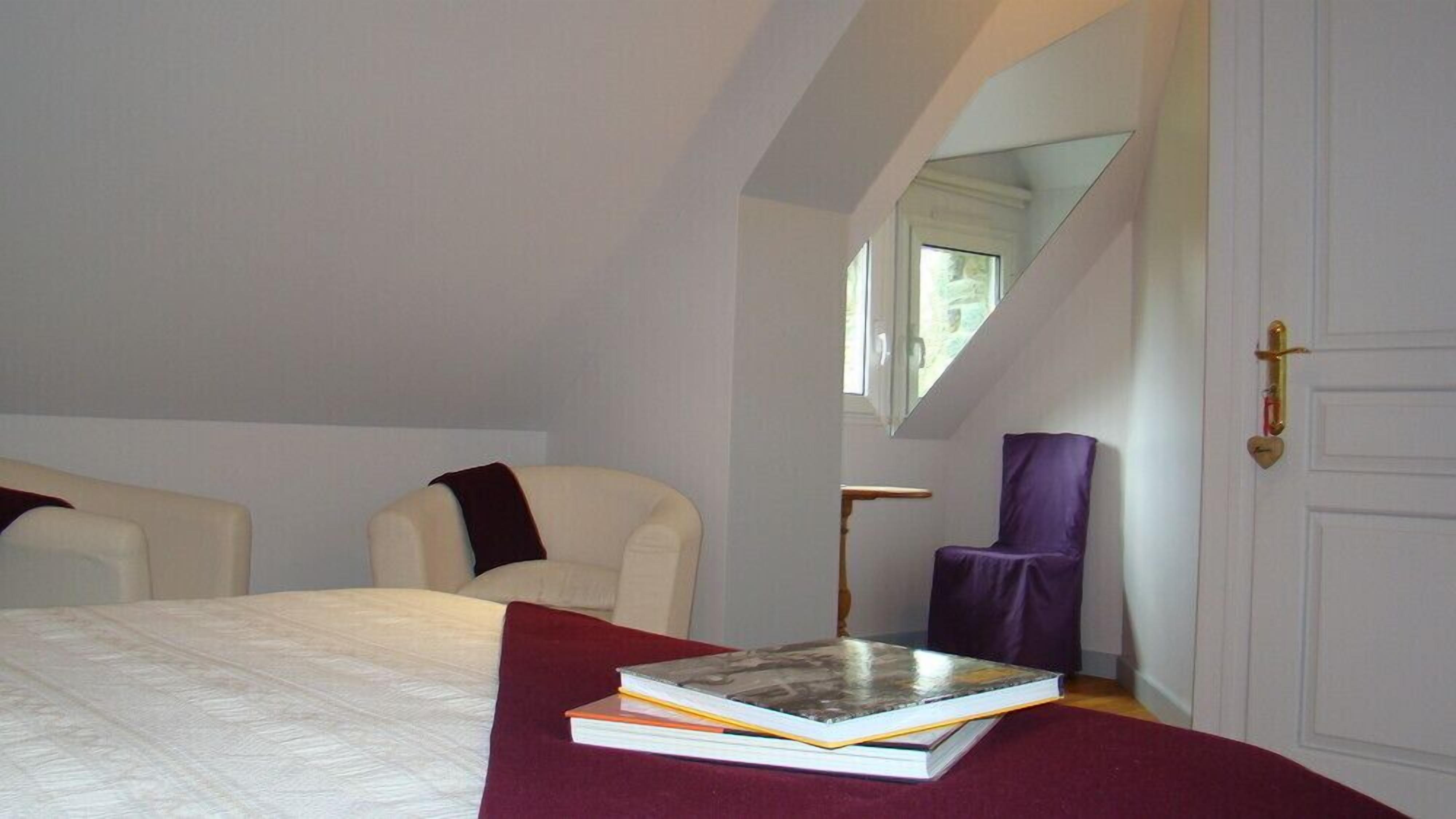 A bedroom with a bed, two chairs, a purple chair, a book, and a mirror.