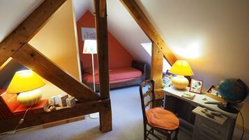 A cozy attic bedroom with a sloped ceiling, wooden beams, a desk with a chair, two lamps, and a globe.